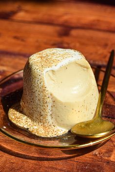 a dessert on a glass plate with a spoon next to it and a wooden table in the background