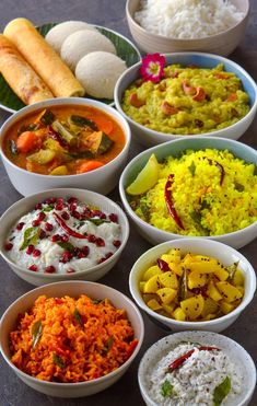 several bowls filled with different types of food on a counter top next to rice and bread