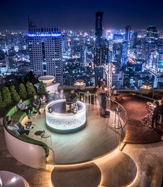 people are sitting at tables on the top of a building with city lights in the background