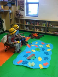 two children sitting on chairs in a room with green flooring and bookshelves