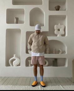 a man standing in front of a white wall with shelves and vases on it