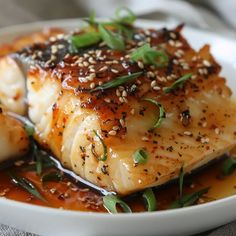 a white plate topped with seared fish covered in sauce and garnished with sesame seeds