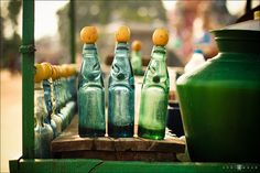 three green bottles sitting on top of a wooden table next to vases and jars