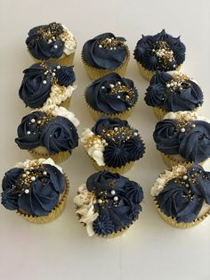 nine cupcakes with blue frosting and gold decorations on them are arranged in rows