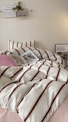 an unmade bed with pink and white sheets, pillows and pictures on the wall