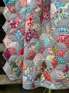 a quilt is hanging up on a wooden bench in front of a fence and flowers