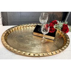 a gold tray with two wine glasses and a book on it next to red roses