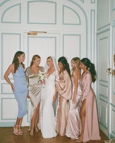 a group of women standing next to each other in front of a white door wearing dresses