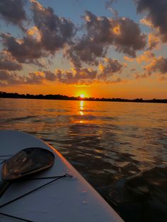 the sun is setting over the water with clouds in the sky and on the boat