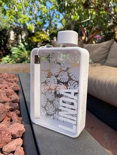 a white bottle sitting on top of a table next to some rocks and trees in the background