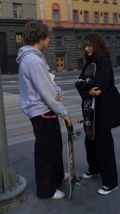 two people standing next to each other with skateboards in their hands on the sidewalk