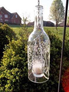 a glass bottle hanging from a chain in front of some bushes and trees on a sunny day