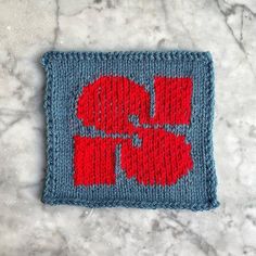 a red and blue knitted square with the word love on it, sitting on a marble surface