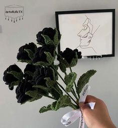 a hand holding a bunch of black flowers in front of a white wall with a drawing on it