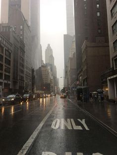 an empty city street in the rain with buildings on both sides and only one way sign painted on the road