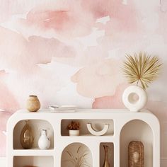 a white shelf with vases and other items on it in front of a pink painted wall