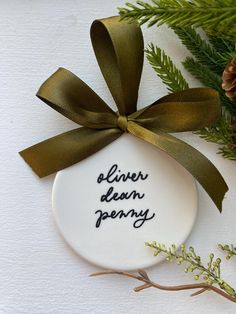 a white ceramic ornament with a green ribbon on it and pine cones in the background