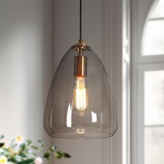 a clear glass light fixture hanging from a ceiling in front of a vase with flowers