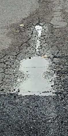 a puddle in the middle of an asphalt road that has been filled with water and rocks