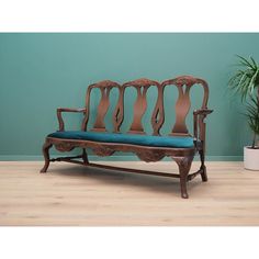 an old wooden bench with blue cushions in front of a green wall and potted plant