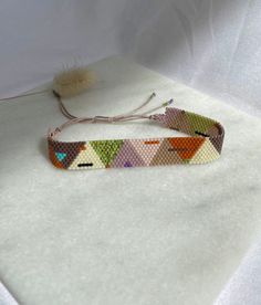 a colorful bracelet is sitting on a white surface with a feather in the middle and an orange bead hanging from it