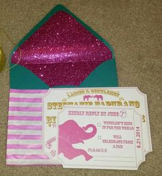 a pink elephant ticket sitting on top of a green envelope next to a purple and white striped ribbon