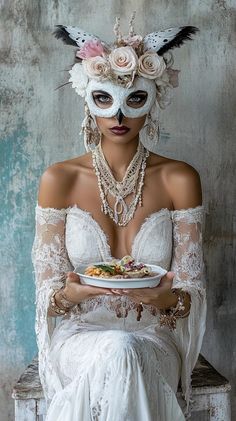 a woman wearing a white mask and holding a plate with food on her chest while sitting in a chair