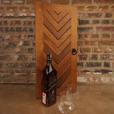 a bottle and two glasses sitting in front of a door with a brick wall behind it