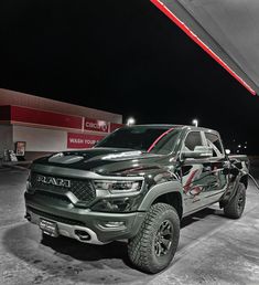 a black and white photo of a truck with red lettering on the hood in front of a gas station