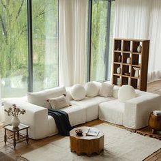 a living room filled with white furniture and large windows overlooking the trees in the distance