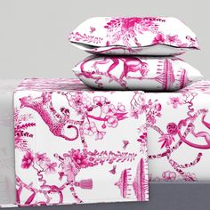 pink and white bedding with decorative designs on the pillow cases, along with matching pillows