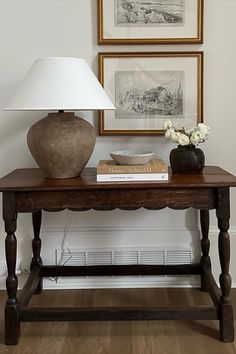 a table with a lamp, vase and books on it