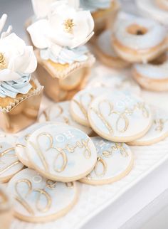 decorated cookies and cupcakes sitting on a table with white flowers in the center