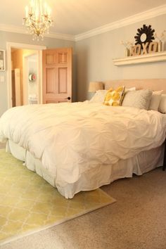 a large white bed sitting inside of a bedroom next to a doorway with a chandelier