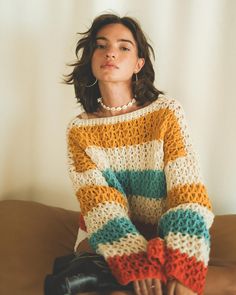 a woman sitting on top of a couch wearing a multicolored knitted sweater