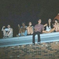 a group of young people sitting on top of a brick wall next to each other