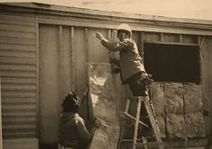 a man standing on a ladder next to a building while another man looks at something