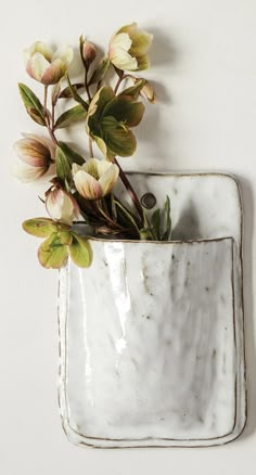 a white vase with flowers in it next to a remote control on the wall,