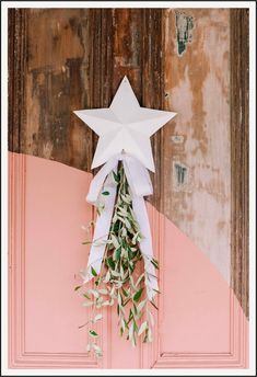 a white star hanging from the side of a door with greenery attached to it