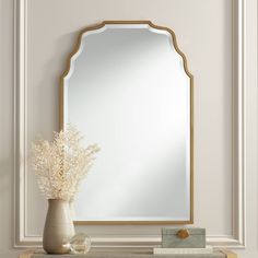 a white vase with flowers and a mirror on top of a dresser in a room