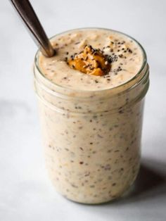 a glass jar filled with food on top of a white table next to a wooden spoon