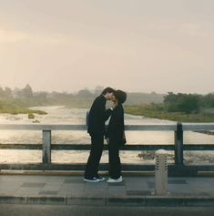 two people standing next to each other in front of a body of water on a bridge