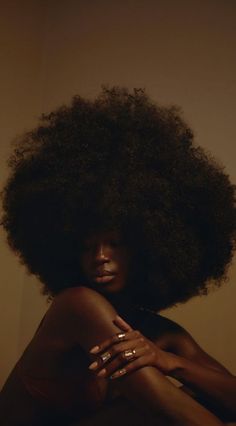 a woman with an afro is sitting on the floor and has her arms folded out