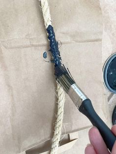 a person holding a paintbrush near a piece of rope