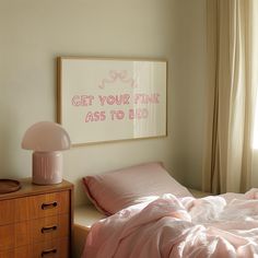 a bed with pink sheets and pillows next to a framed art piece on the wall