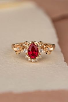 a close up of a ring with a red stone in the middle and two gold leaves around it