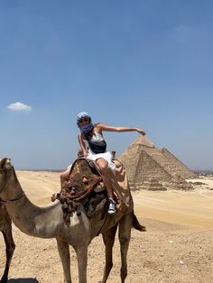 a woman riding on the back of a camel next to pyramids in the desert