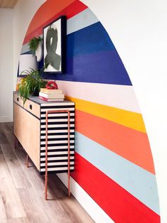 a colorful wall with a wooden cabinet and plant on it in front of a mirror