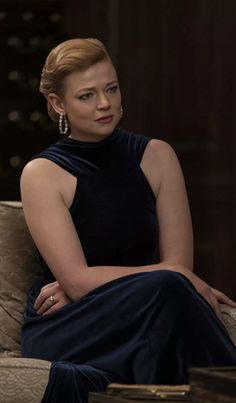 a woman sitting on top of a couch wearing a black dress and diamond earring