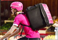 a man riding a bike with a pink shirt on and a black bag on his back